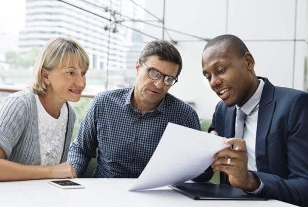 Insurance Companies - An Agent in a Suit Explains Options to Clients, a Mature Couple, in an Office Filled with Large Windows